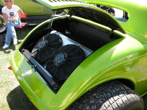 1998 Ford Crown Victoria - Rear-hinged decklid of a lime-green metalflake custom car open to reveal two large black electric cooling fans, with a seated spectator nea…
