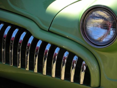 1998 Ford Crown Victoria - Detail of a lime-green custom car showing its vertical chrome grille bars and a single round headlight reflecting the surroundings.