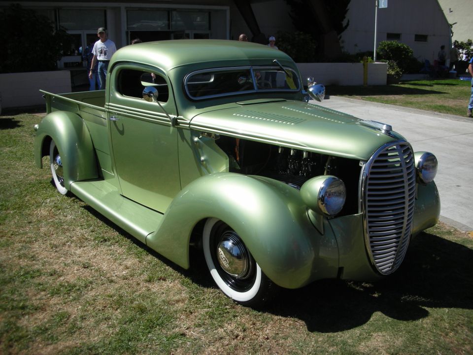 Green vintage pickup hot rod with split windshield and whitewall tires on grass