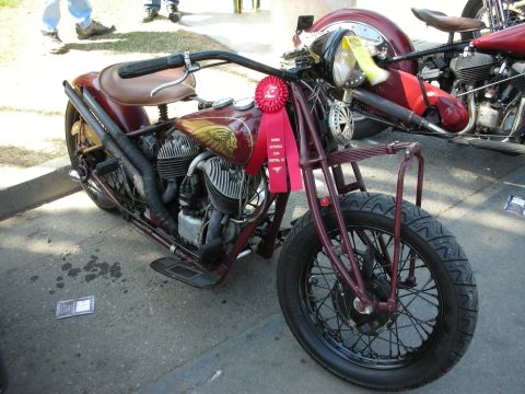 1998 Ford Crown Victoria - maroon vintage motorcycle with a sprung leather seat and a red award ribbon attached to its fuel tank, parked on pavement at a show.