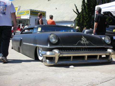 1998 Ford Crown Victoria - heavily chopped and lowered satin-black custom car with delicate pinstriping and bullet bumper guards sits among onlookers at an outdoor sh…