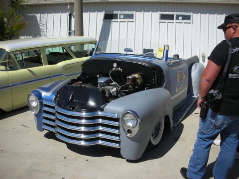 1998 Ford Crown Victoria - gray custom hot rod pickup sits with its hood open exposing a chrome-topped V8, a man standing beside it at an outdoor show.