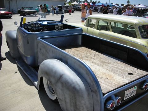 1998 Ford Crown Victoria - bare-metal lowered roadster pickup with a wood-plank bed floor and club plaque, parked among classic cars at a crowded show.