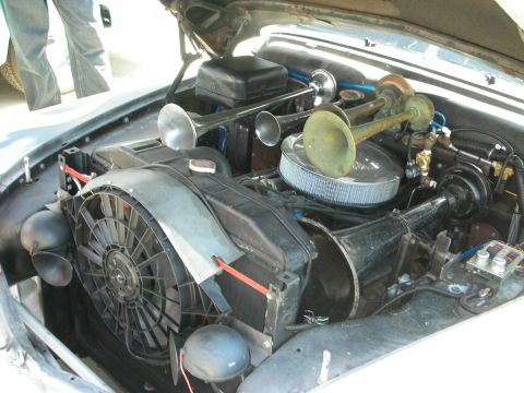 1998 Ford Crown Victoria - engine bay showing a chrome air cleaner, large dual chrome air horns, and an electric radiator fan in a vintage car.