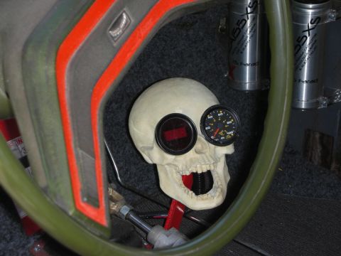 1998 Ford Crown Victoria - novelty skull mounted on a car dashboard cradles a digital readout and a round gauge, viewed through a green steering wheel.