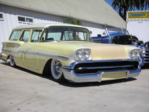 1998 Ford Crown Victoria - pale-yellow lowered late-1950s station wagon with quad headlights and a heavy chrome grille parked at an outdoor show.