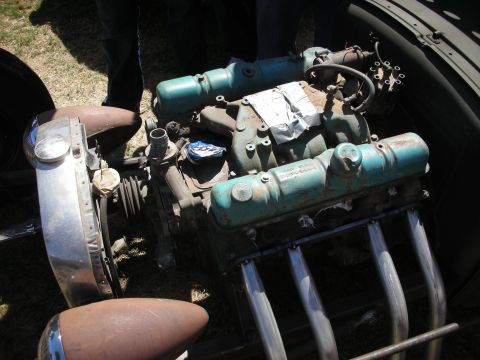 1998 Ford Crown Victoria - vintage flathead V8 with teal-painted heads sits in an open engine bay beneath a chrome bumper and single headlight.