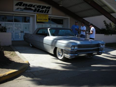 1998 Ford Crown Victoria - silver early-1960s Cadillac coupe parked outside Anacapa Hall, where an Oldies Show banner hangs above the doors.