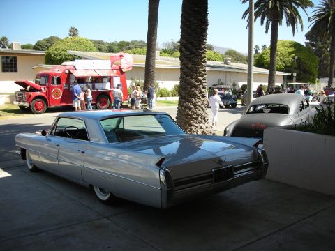 1998 Ford Crown Victoria - rear quarter of a silver 1960s Cadillac with a vintage red fire truck and palm trees behind it at an outdoor show.
