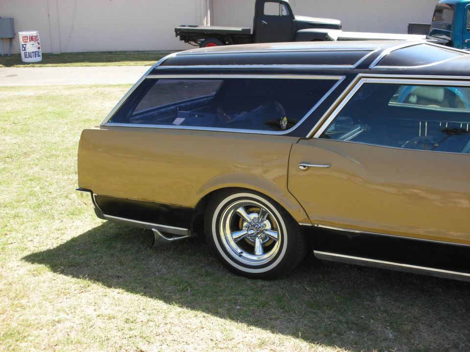 Rear quarter of gold black-roof station wagon with chrome wheels, pickup behind