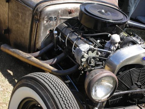 1998 Ford Crown Victoria - exposed V8 with a chrome air cleaner and swept headers powers a bare-metal rat rod, a whitewall tire in the foreground.