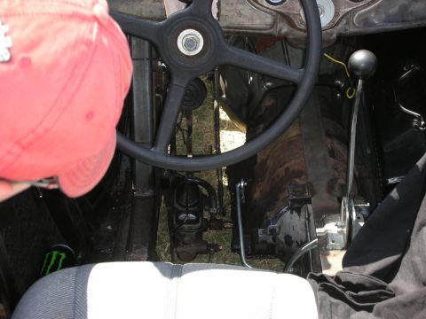 1998 Ford Crown Victoria - man in a red cap works inside the bare cockpit of a hot rod, with a black steering wheel, floor shifter, and exposed pedal assembly.