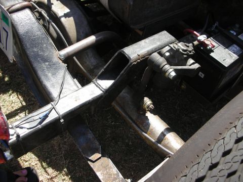 1998 Ford Crown Victoria - Detail of a fabricated front suspension on a hot rod showing welded tube framework, a leaf spring, steering linkage, and a battery.