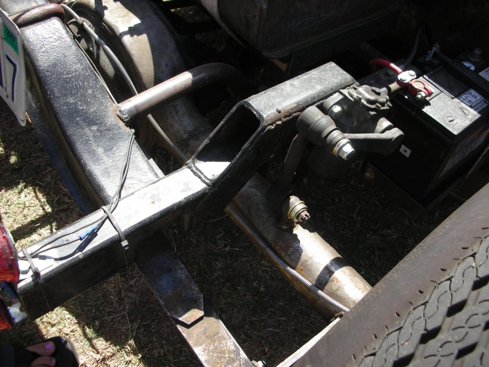 Close-up of welded tube chassis with leaf spring, drag link, and battery on a hot rod