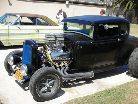 1998 Ford Crown Victoria - black 1930s-style five-window hot rod coupe sits on grass with an exposed chrome-topped V8 engine and zoomie-style headers.