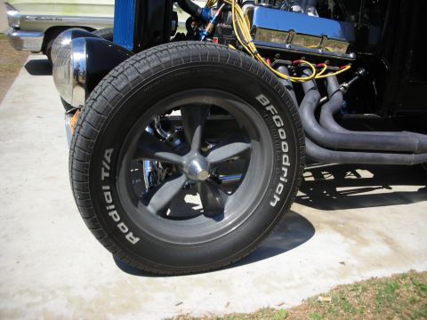 1998 Ford Crown Victoria - Close-up of a hot rod's front wheel fitted with a gray five-spoke mag wheel and a BFGoodrich Radial T/A white-letter tire, beside chrome he…