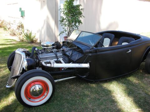 1998 Ford Crown Victoria - black 1930s-style roadster hot rod rests on a lawn with an exposed V8 engine, white-and-black tuck interior, and red wheels with whitewall…