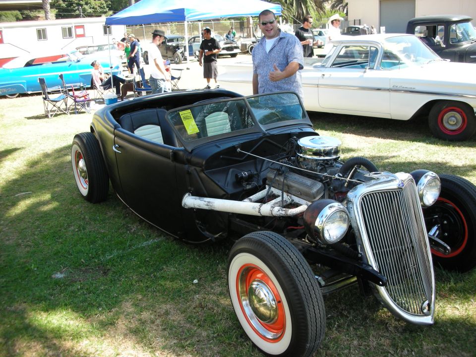 Black highboy roadster hot rod at car show with man giving thumbs up nearby