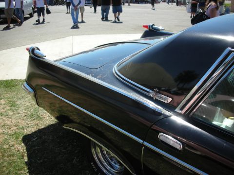 1998 Ford Crown Victoria - rear quarter and roofline of a glossy black 1960s hardtop coupe with chrome window trim, photographed at a car show.