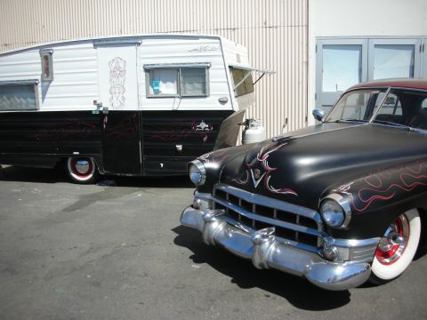 1998 Ford Crown Victoria - matte-black 1940s Cadillac with red flame graphics and whitewalls parked beside a matching black-and-white pinstriped vintage travel traile…