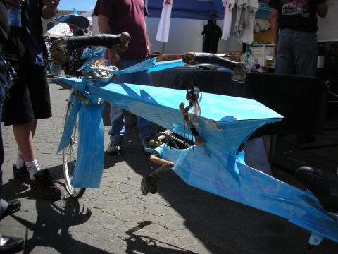 1998 Ford Crown Victoria - custom art bicycle painted bright blue with angular fin-like bodywork and bone and skeleton decorations on display at a street fair.