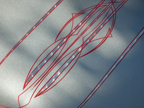 1998 Ford Crown Victoria - Detail of delicate red pinstriping in a symmetrical leaf-and-fish design on a silver metallic car panel lit by sunlight.