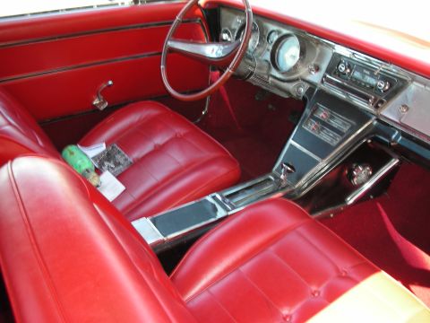 1998 Ford Crown Victoria - Interior of a 1960s coupe with bright red vinyl bucket seats, a chrome center console, sport steering wheel, and integrated dash gauges.