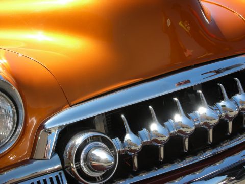 1998 Ford Crown Victoria - Tight detail of a copper-orange custom car showing its glossy fender, chrome bullet-tooth grille, and round headlight bezel.