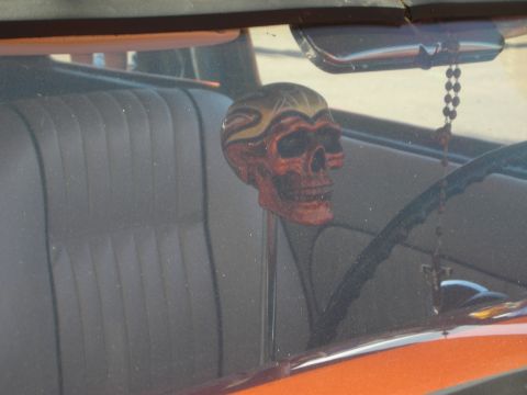 1998 Ford Crown Victoria - flame-painted skull-shaped gear shift knob mounted on a column inside a custom car, viewed through the side window with a bead chain hangin…