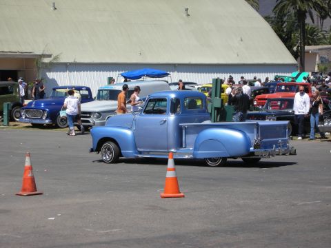 1998 Ford Crown Victoria - light-blue late-1940s/early-1950s pickup truck, lowered with a chrome rear bumper, parked between traffic cones at a crowded car show.