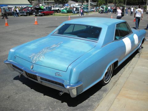 1998 Ford Crown Victoria - Rear three-quarter view of a light-blue 1960s coupe with white pinstriping and a lowered stance in a busy car show parking lot.