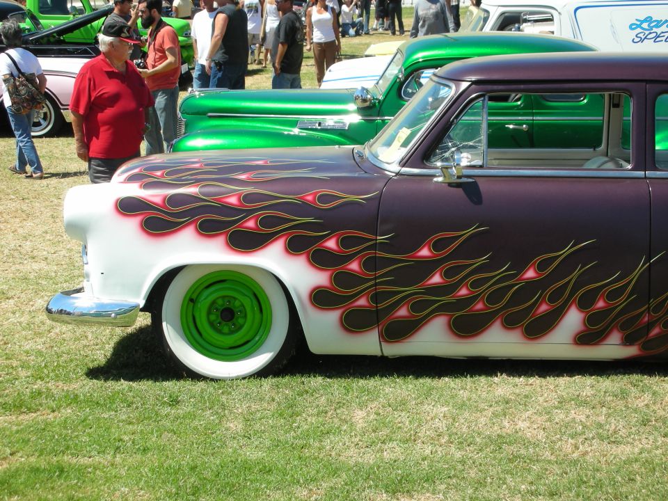 Purple and white 1950s sedan with flame paint and green wheels at car show