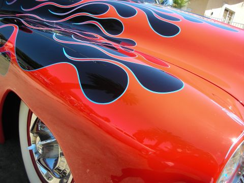 1998 Ford Crown Victoria - Detail of a glossy red fender painted with black flames outlined in blue, above a chrome wheel and whitewall tire.