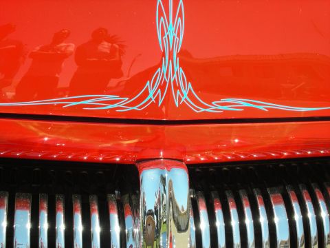 1998 Ford Crown Victoria - Close-up of a red car nose with symmetrical teal pinstriped scrollwork above a polished chrome grille.