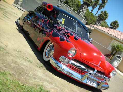 1998 Ford Crown Victoria - Front three-quarter view of a chopped red custom car with black flames, whitewalls and HERCULA plate on a sunny lot.