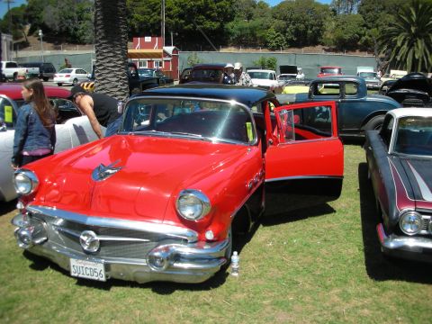 1998 Ford Crown Victoria - red 1950s hardtop with its door open showing the interior, parked among classic cars at an outdoor show; plate SUICD56.