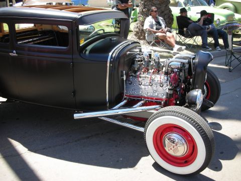 1998 Ford Crown Victoria - flat-black channeled coupe hot rod displays its polished V8 engine and red steelie with whitewall tire at a car show.
