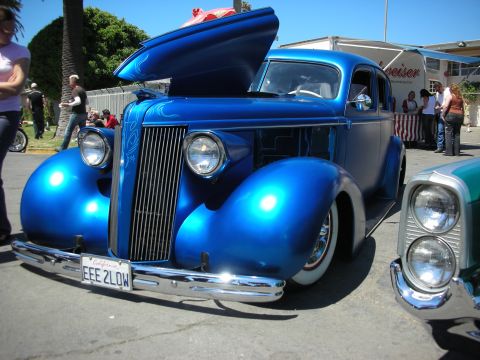 1998 Ford Crown Victoria - bright blue chopped 1930s coupe with its hood up and chrome grille on display at an outdoor car show; plate EEE 2LOW.