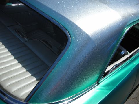 1998 Ford Crown Victoria - Detail of a custom car's teal-green metalflake paint over the roofline and rear quarter window, with white pleated upholstery visible insid…