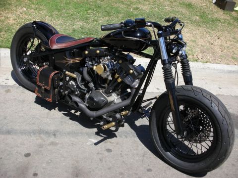 1998 Ford Crown Victoria - black bobber-style custom motorcycle with a sprung solo seat, leather saddlebag and exposed V-twin engine parked on asphalt.
