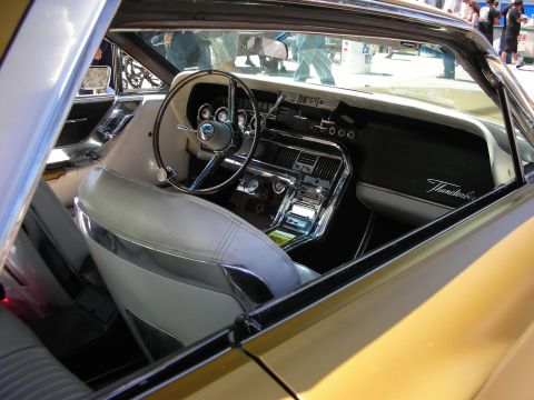 1998 Ford Crown Victoria - Interior of a gold 1960s Ford Thunderbird with white seats, dashboard gauges and chrome 'Thunderbird' script on the glovebox.