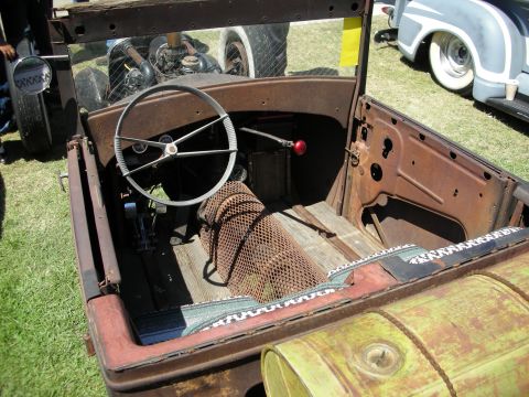 1998 Ford Crown Victoria - weathered interior of a vintage open roadster project showing a banjo steering wheel, mesh-wrapped column and wooden floorboards.