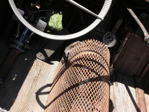 1998 Ford Crown Victoria - Detail of an aged steering column wrapped in rusty expanded-metal mesh above wooden floorboards inside an open vintage car.