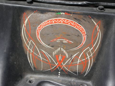 1998 Ford Crown Victoria - Hand-painted pinstripe artwork depicting a mustachioed face wearing a sombrero, done in red and white on weathered black metal.