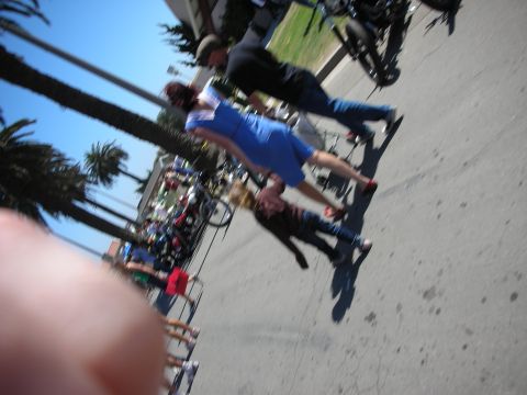 1998 Ford Crown Victoria - blurred candid shot of a woman in a blue dress holding a child's hand as they walk past parked motorcycles at an outdoor show.
