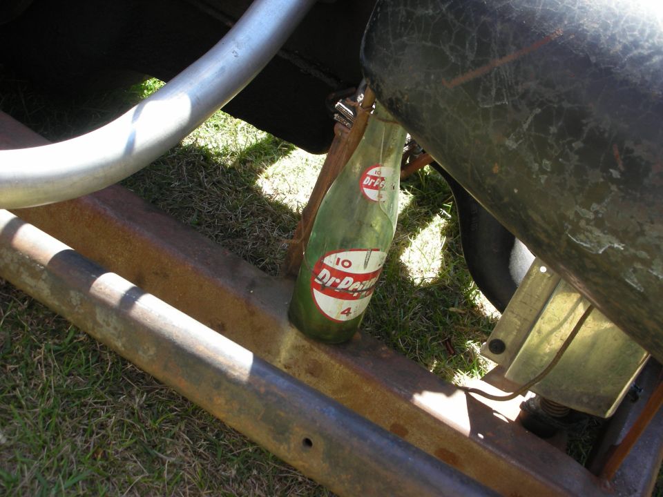 Vintage Dr Pepper glass bottle resting on a rusty car frame rail