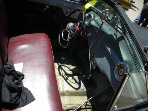 1998 Ford Crown Victoria - Interior of a customized car showing a red bench seat, a small chain-style steering wheel and a worn painted floor.