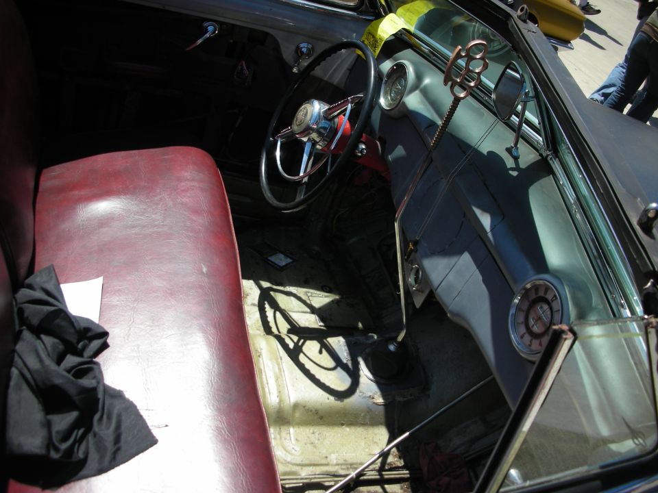 Interior of a custom car with red bench seat and small chained steering wheel