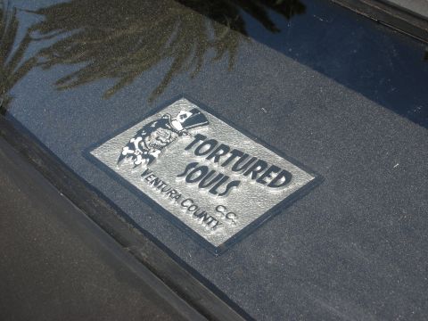 1998 Ford Crown Victoria - polished metal car-club plaque engraved 'TORTURED SOULS C.C. VENTURA COUNTY' with a skull mascot, set on textured black paint.