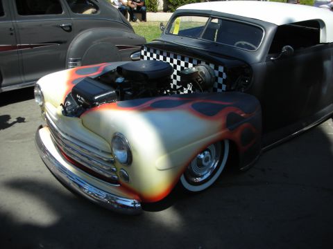 1998 Ford Crown Victoria - lowered hot rod with cream-and-orange flame paint, whitewall tires, and an exposed supercharged engine sits at an outdoor car show.
